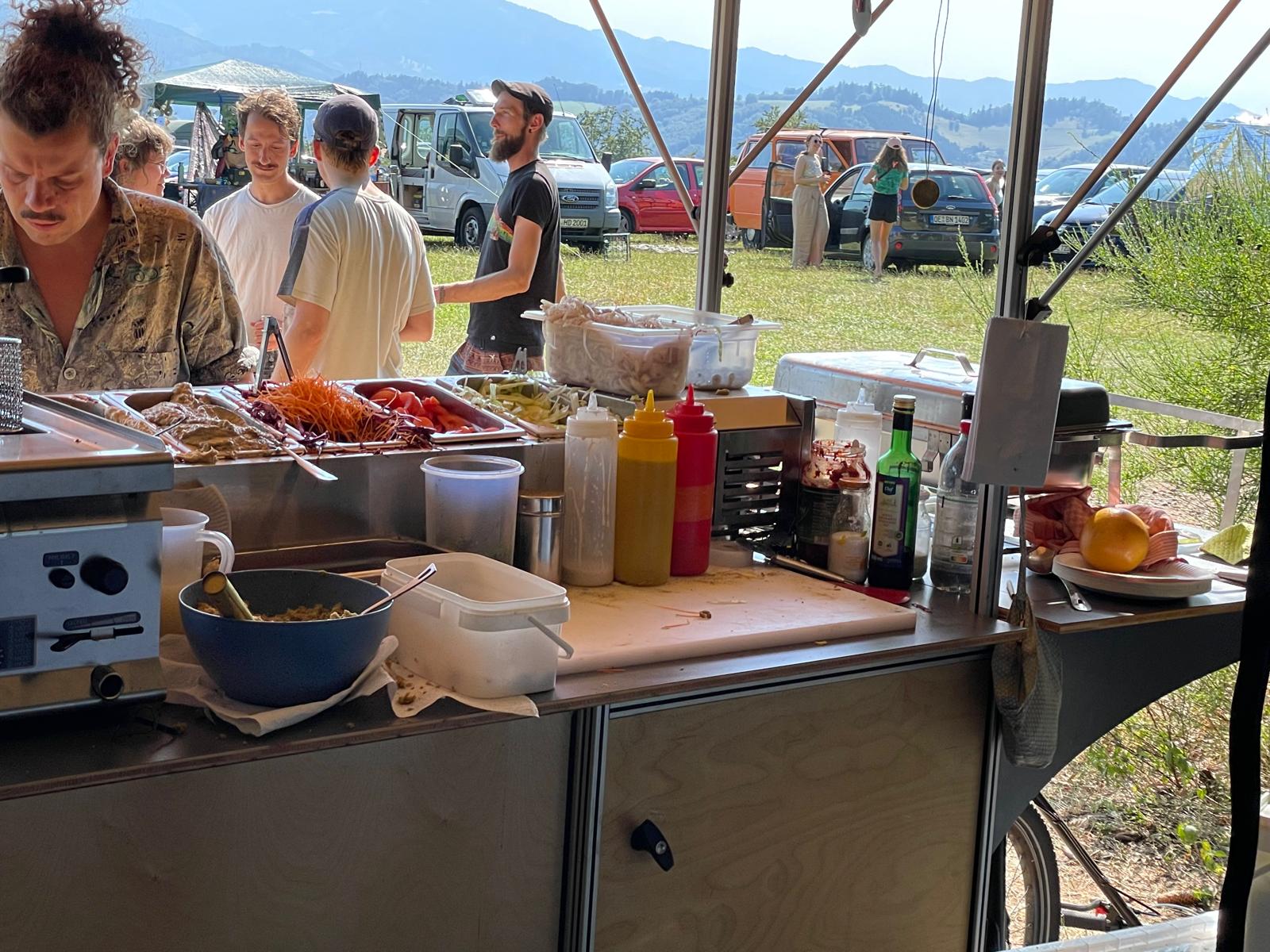 Gäste am Streetfood-Stand mit Bergpanorama im Hintergrund